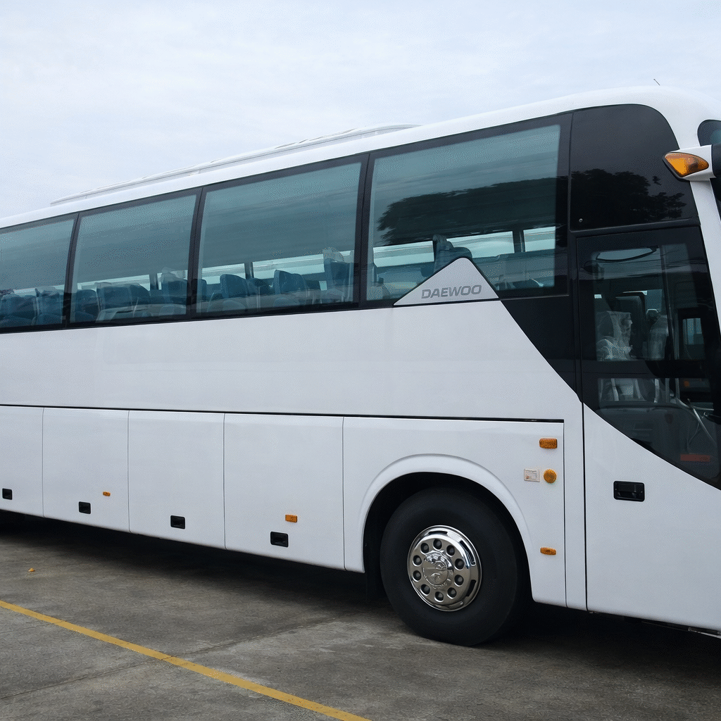White coach bus parked on a concrete lot under a cloudy sky, with large tinted windows and side storage compartments visible.